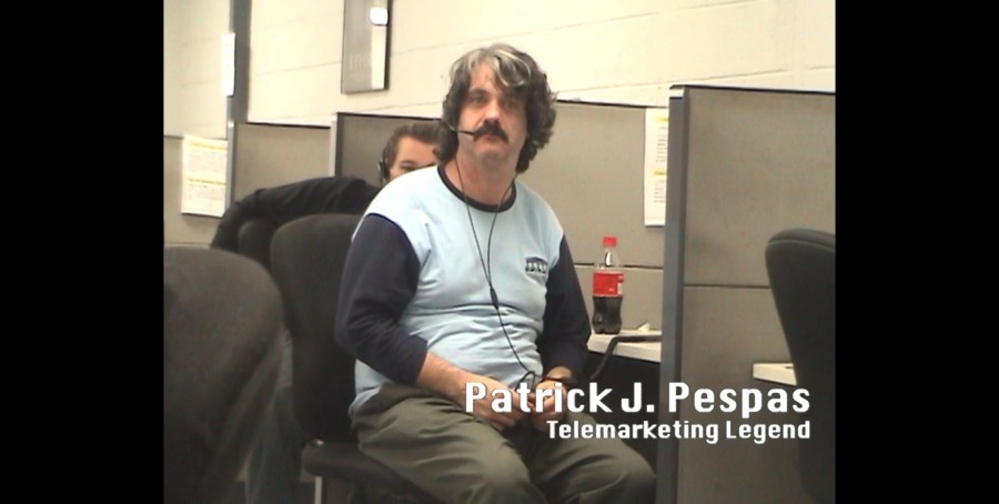 Middle aged man with greying hair and mustache works from his cubicle at a telemarketing call center