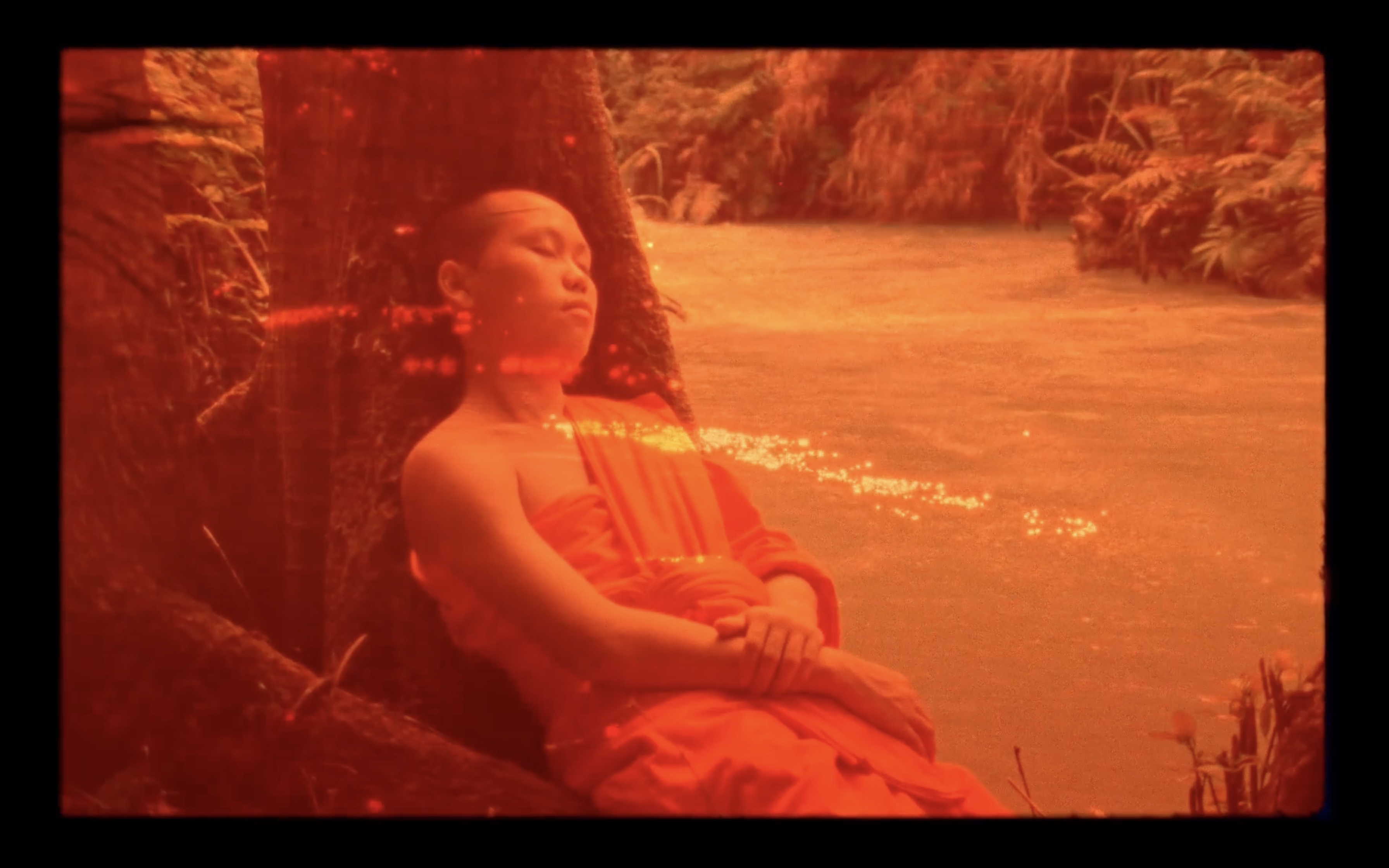 a young asian man in robes is sleeping by a river