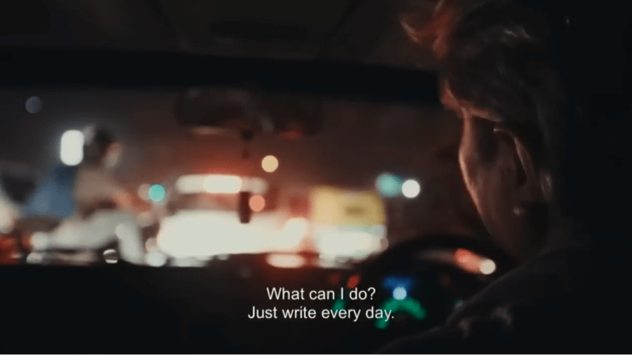 dark interior of a car; the driver's head, from the perspective of the back seat. Taillights tint the image read