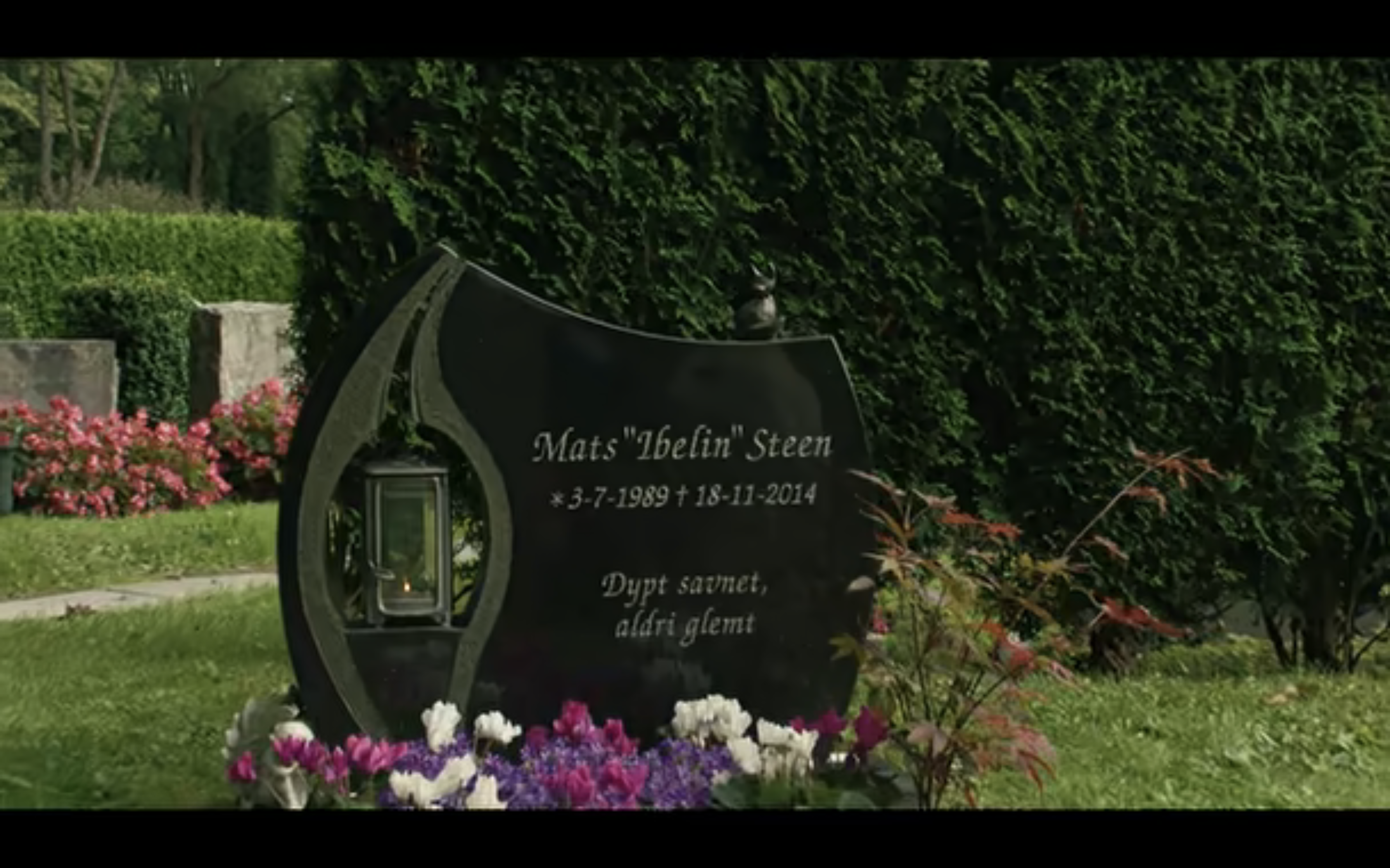 a dark, granite gravestone marker with colorful flowers planted around the base